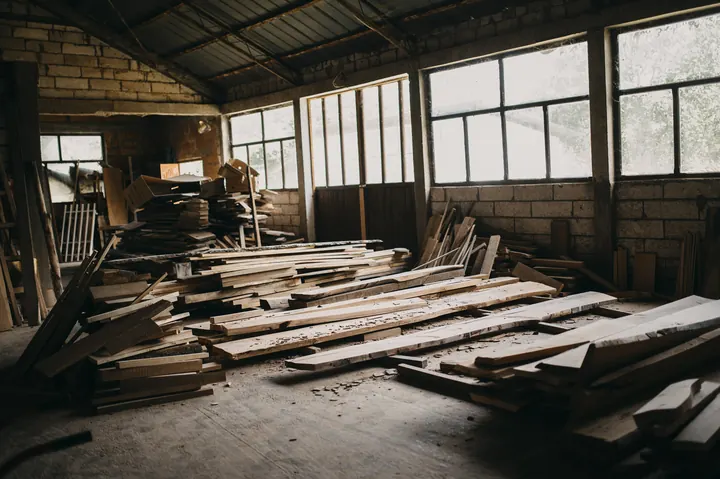 Atelier de menuiserie éclairé par de grandes fenêtres, planches de bois empilées au sol