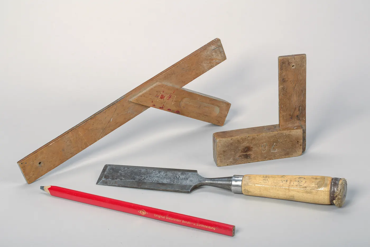 Deux équerres de menuisier, un ciseau à bois et un crayon de charpentier sur fond blanc