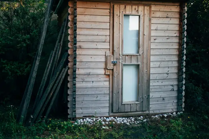Façade d'un abri en planches de bois brut avec une porte vitrée, en forêt