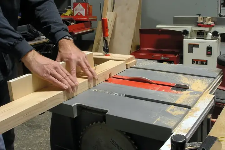 Mains guidant une planche sur une scie sur table pour tailler un assemblage