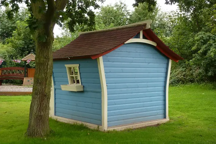Cabane d'enfant en bois peinte en bleu et blanc, sous un arbre dans un jardin