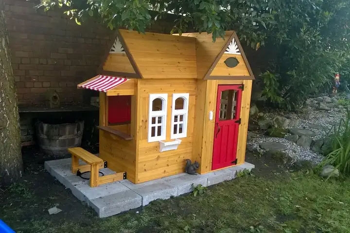 Maisonnette d'enfant en bois verni avec porte rouge, posée sur des dalles