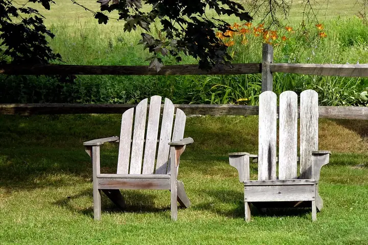 Deux fauteuils Adirondack en bois sur une pelouse, devant une clôture