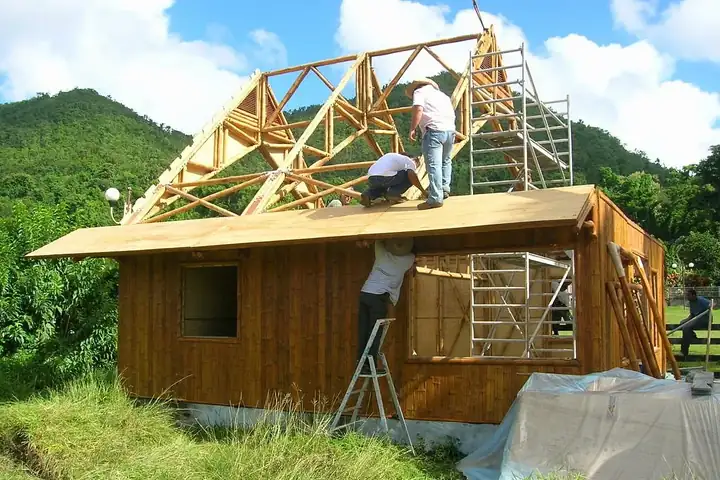 Ouvriers posant les fermes de charpente sur une petite maison à murs en bois