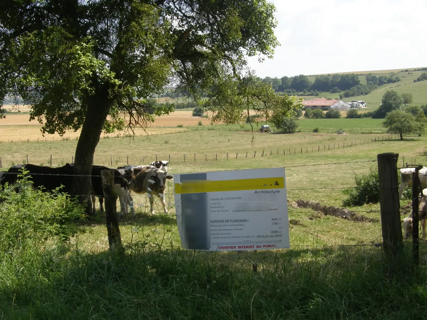 Panneau d'affichage d'un permis de construire planté en bordure d'un pré