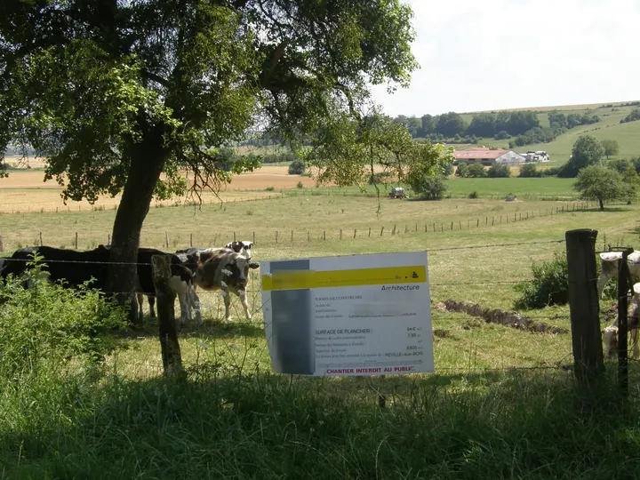 Panneau d'affichage d'un permis de construire planté en bordure d'un pré