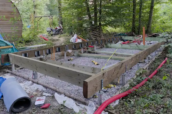 Cadre de plancher en bois posé sur des pieux vissés métalliques, en cours de construction sur un lit de gravier