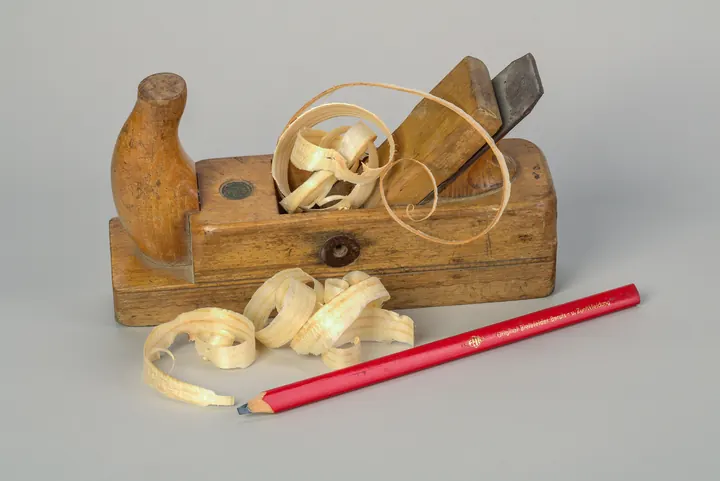 Rabot en bois entouré de copeaux, avec un crayon de charpentier rouge